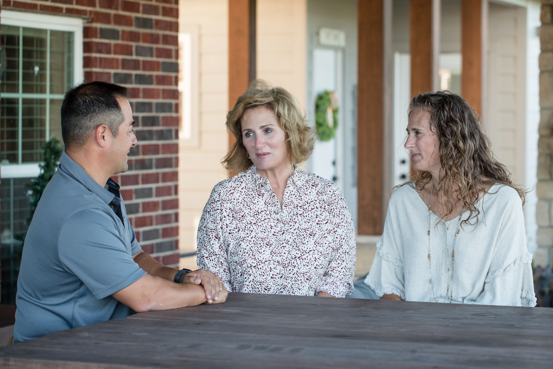Connie Scott sitting at a table talking with two Nueces County residents on a front porch
